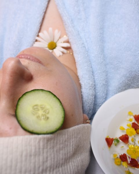 woman wearing blue robe lying with cucumber on eye