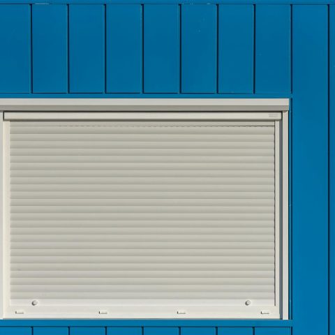 A modern blue wall with a closed white roller shutter, perfect for architectural designs.