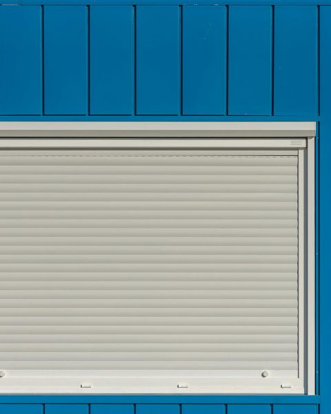 A modern blue wall with a closed white roller shutter, perfect for architectural designs.