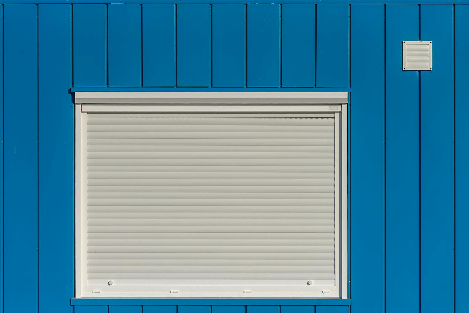A modern blue wall with a closed white roller shutter, perfect for architectural designs.