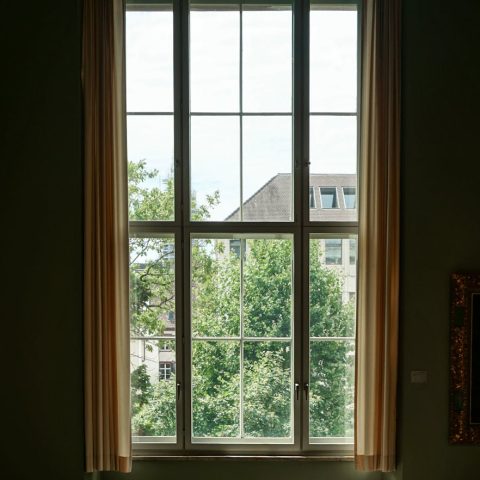 Sunny room with large window overlooking greenery and cityscape.