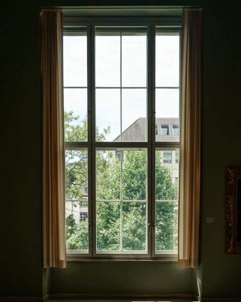 Sunny room with large window overlooking greenery and cityscape.