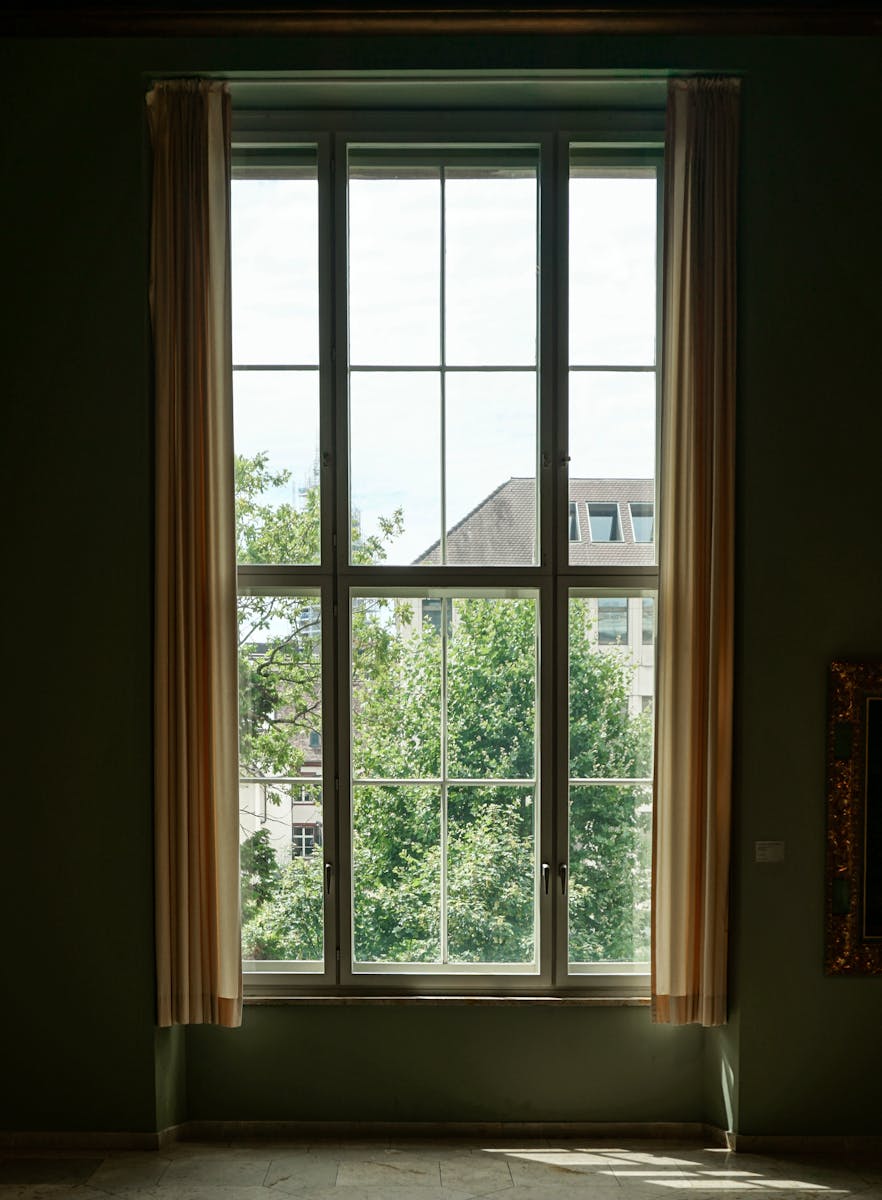 Sunny room with large window overlooking greenery and cityscape.