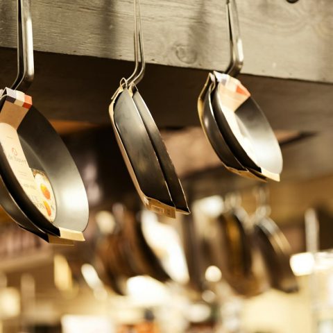 A selection of frying pans hanging in a kitchenware shop for sale.