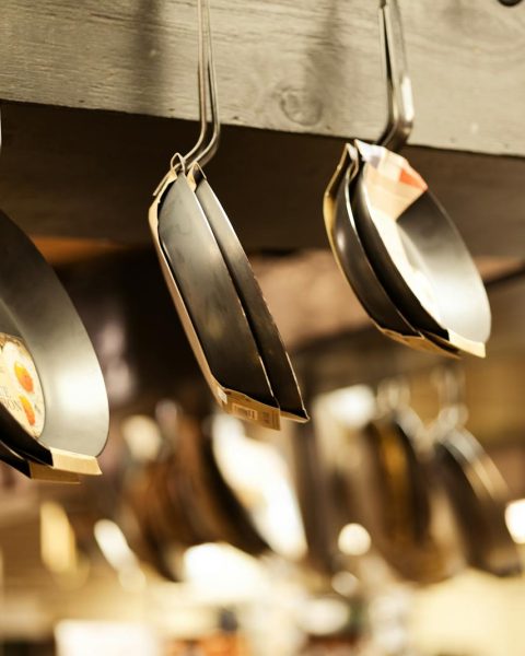 A selection of frying pans hanging in a kitchenware shop for sale.