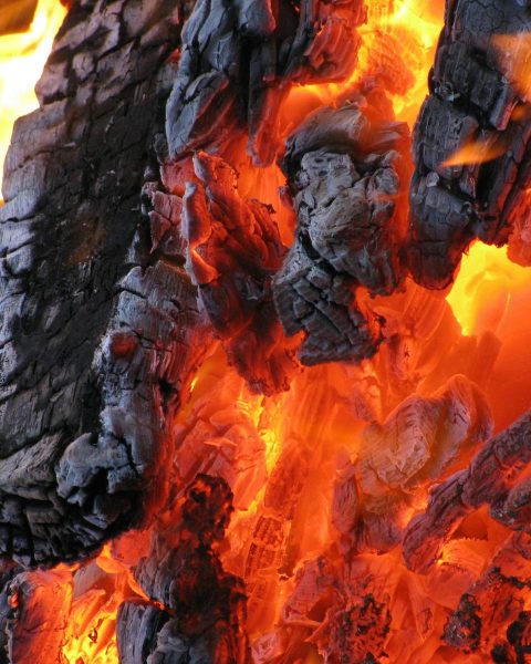 Detailed view of hot embers and flames from burning charcoal. A vibrant display of fire and heat.