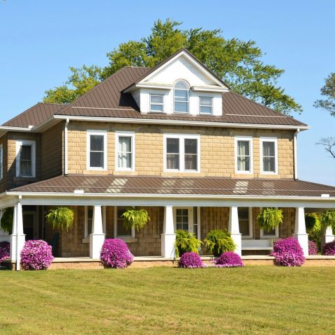 A tan two-story farmhouse with a wrap-around porch