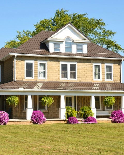 A tan two-story farmhouse with a wrap-around porch
