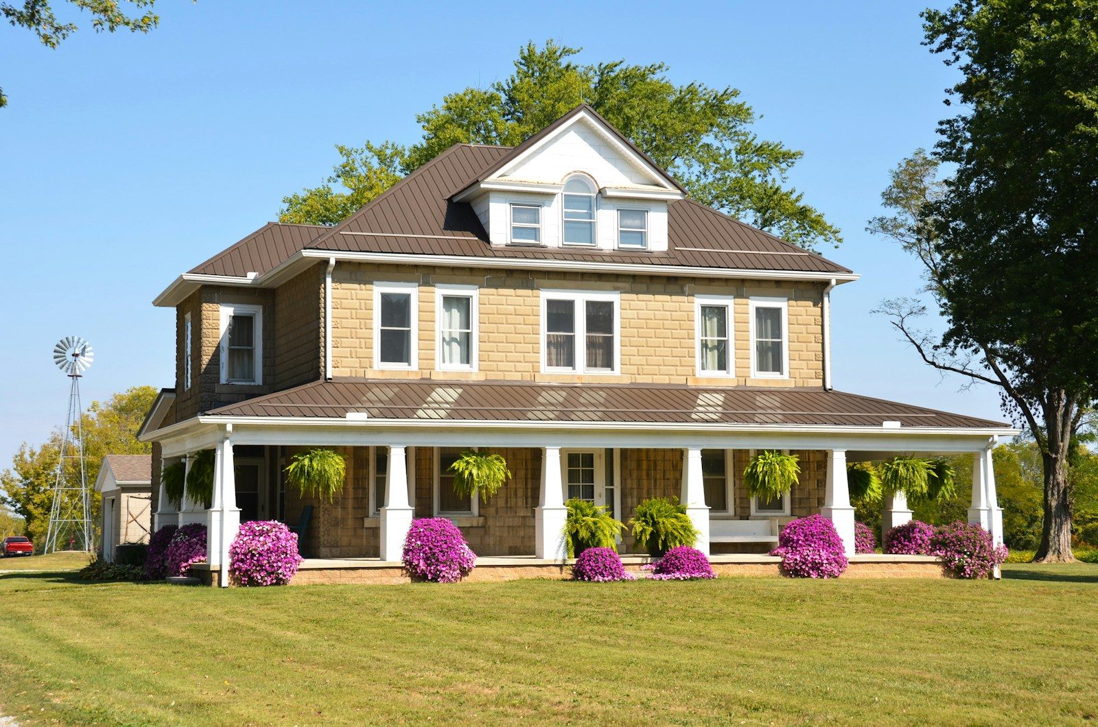 A tan two-story farmhouse with a wrap-around porch