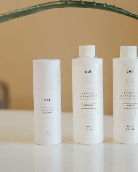three bottles of lotion sitting on a table next to a potted plant