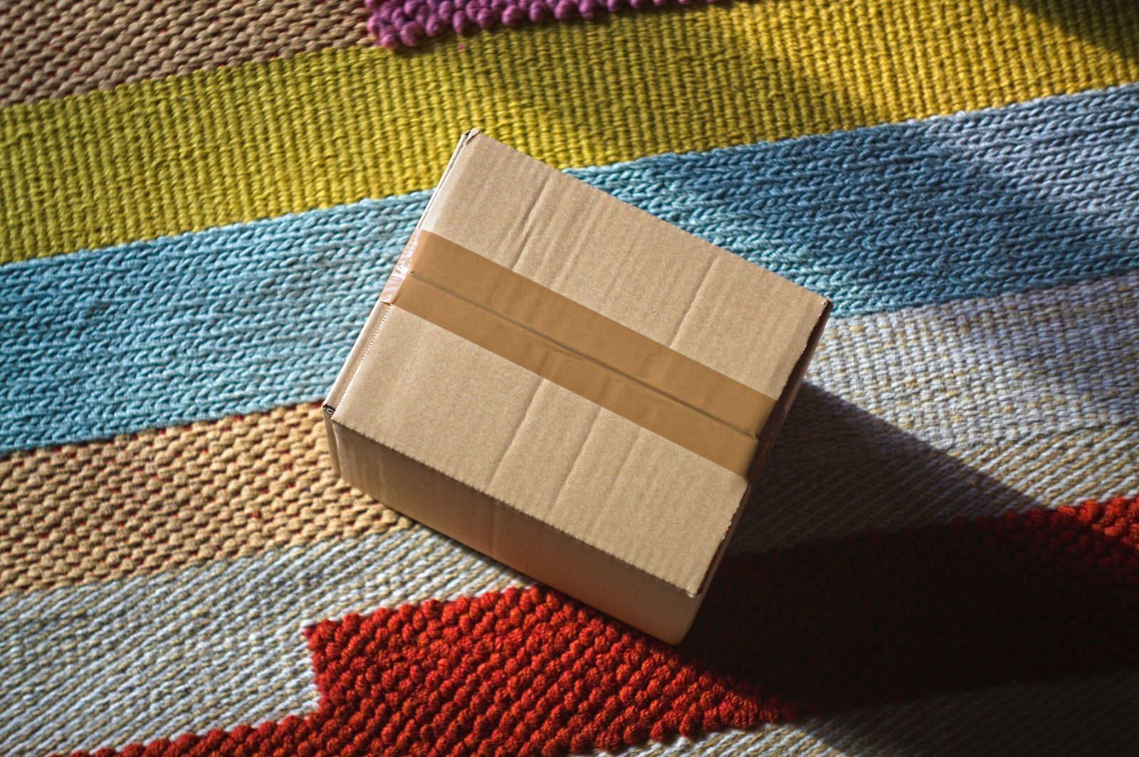 A closed cardboard box sits on a striped rug