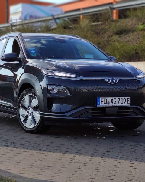 Gezin met kinderen die bagage laden in een elektrische SUV op de oprit